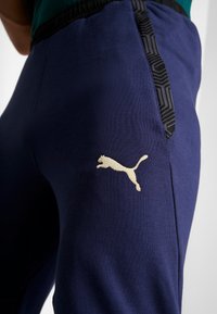Marineblauwe sweatpants van zacht materiaal. Bevat een gestructureerd zwart zijpaneel en een gouden Puma-logo op de bovenbeen. Elastische tailleband voor comfort.