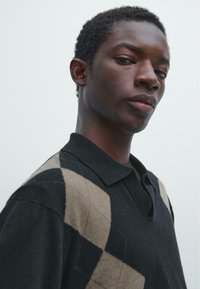 Zwart poloshirt met diamantpatronen in beige, voorzien van een kraag en korte mouwen, gemaakt van een zachte, gestructureerde stof.