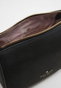 Černá kožená kosmetická taška se zlatým zipem. Interiér je vybaven hladkým růžovým podšívkou a jemným tečkovaným vzorem. Logo je umístěno na vnějšku.