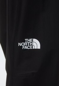 Pantalons noirs en matériau léger avec un logo blanc "The North Face" et un design en demi-lune caractéristique sur la cuisse.