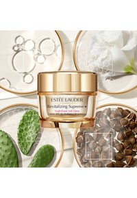 Revitalisierende Supreme+ Youth Power Soft Crème in einem klaren Glas mit goldenen Akzenten. Umgeben von grünen Kaktusblättern und dekorativen weißen Tellern.