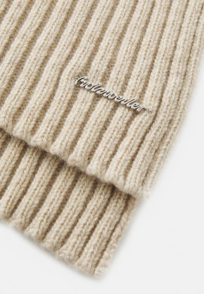 Căciulă tricotată bej cu model cu nervuri, fabricată din material moale, având un eticheta cu logo argintiu. Textura este caldă și confortabilă, cu margini drepte.