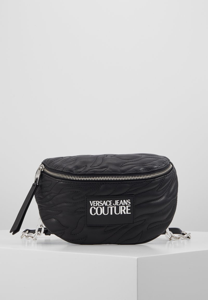 Svart quiltad handväska med dragkedjestängning, prydd med en framträdande logotypapplikation, silverdetaljer och en rundad, kompakt form.