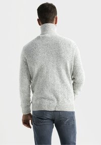 Maglione grigio chiaro a maglia con colletto alto, tessuto strutturato e polsini e orlo a costine. Indossato con jeans grigio scuro, visto da dietro.