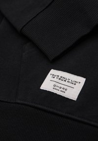 Il tessuto della felpa nera presenta un collo e polsini a coste, con un'etichetta bianca che riporta il testo: "IL TUO UNICO LIMITE È LA TUA MENTE" e "OMBRE dal 1985."