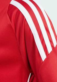 Maglietta sportiva rossa con strisce bianche sulle spalle, realizzata in tessuto liscio e morbido con una silhouette aderente.