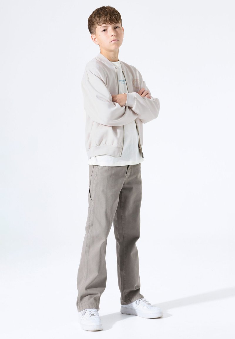 Chaqueta bomber gris claro con ribete acanalado, combinada con una camiseta blanca y pantalones gris claro. Los accesorios incluyen zapatillas blancas.