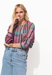 Chemise à carreaux multicolores en tissu léger, avec des manches longues, un devant à boutons et une poche sur le côté gauche. Associée à un short en denim.