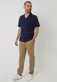 Camisa de manga corta navy con cuello, botones al frente, combinada con pantalones chinos marrón claro y zapatillas blancas. Ajuste simple y entallado.