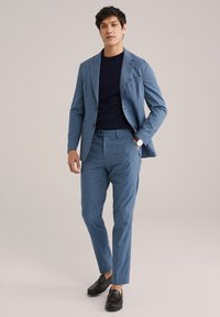 Lichtblauw pak met een textuurstof, een getailleerde blazer, slanke broek en een marineblauwe crew-neck shirt. Gecombineerd met zwarte loafers.