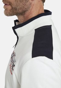 White cotton sweatshirt with navy accents, ribbed collar, and embroidered logo. Features a half-zip and textured fabric design.