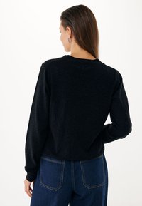 Maglione nero con scollatura rotonda e maniche lunghe. Texture morbida e vestibilità rilassata. Abbinato a pantaloni in denim a vita alta di colore blu scuro.