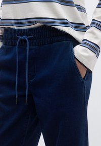 Pantalones jogger azul marino hechos de tela suave, con cinturilla elástica, cordón y bolsillos laterales, combinados con una camiseta de manga larga a rayas.