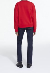 Sudadera roja con cuello redondo y ribete en el dobladillo, combinada con jeans ajustados de color azul oscuro y botas negras hasta el tobillo.