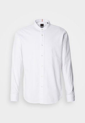 Camisa blanca de manga larga con cuello de banda, cierre de botones en el frente y dobladillo redondeado. Hecha de algodón, presenta una textura suave y un brillo sutil.