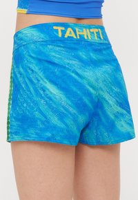 Modré sportovní šortky s texturovaným, vlnkovitým vzorem. Mají žlutý pás s nápisem "TAHITI" a zelené boční akcenty.
