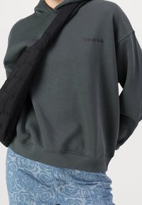 Sudadera de un verde oscuro con un corte holgado, que presenta una tela texturizada y texto bordado. Combinada con unos vaqueros azules decorados con un patrón de rosas.