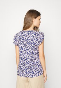 Blusa de manga curta com um padrão abstrato azul e rosa, apresentando detalhes de ombreira com ruffles e um decote redondo. Textura de tecido suave.