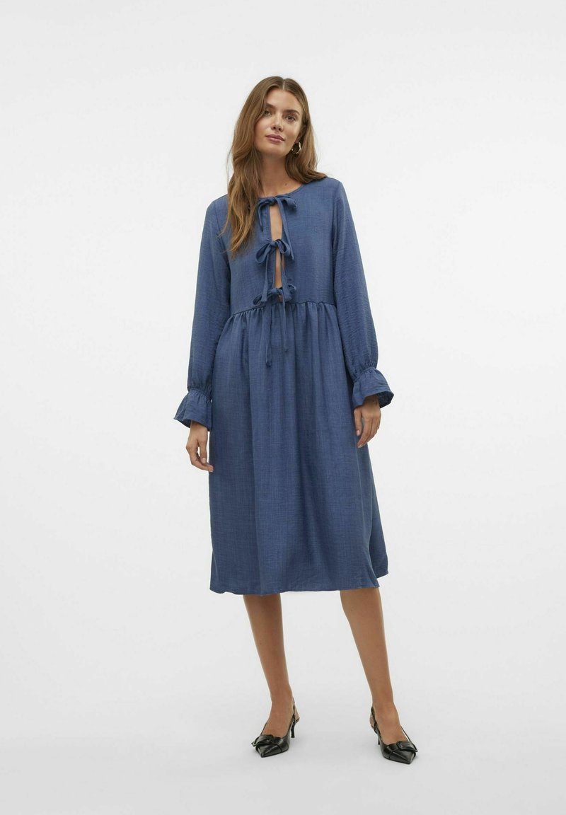 Modra obleka z dolgimi rokavi in poudarjenim pasom, z vezanjem spredaj in teksturirano tkanino. Ima nagubane rokave in midi dolžino.