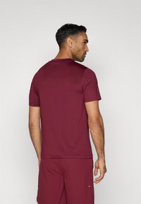 Trumpas marškinėliai su trumpomis rankovėmis, bordo spalvos, su apvaliu iškirpimu, lygi texture ir šiek tiek prigludusia danga. Galinis vaizdas rodo peties siūlų detales.