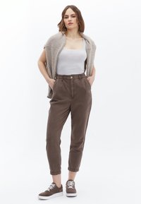 Světlé hnědé chinos s elastickým pasem a předním knoflíkem, s bočními kapsami a zúženými kotníky. V paré s šedým pleteným šátkem.