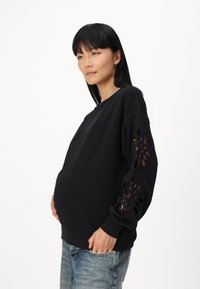 Black sweatshirt with cut-out floral designs on the sleeves, loose fit, soft texture, paired with light blue distressed jeans.