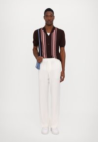 Cămașă bej cu mânecă scurtă și dungi verticale roz, asortată cu pantaloni albi cu șnur și adidași albi; geantă albastră purtată pe umăr.