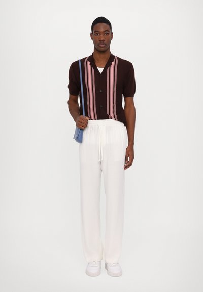 Short-sleeved brown shirt with pink vertical stripes, paired with white drawstring pants and white sneakers; blue bag slung over shoulder.