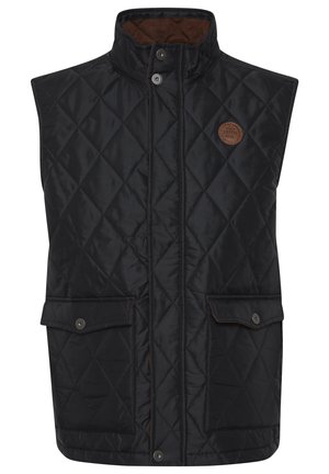 Vesta neagră matlasată cu guler înalt, închidere cu capse și două buzunare în față. Dispune de un interior maro și o etichetă rotundă a mărcii pe piept.