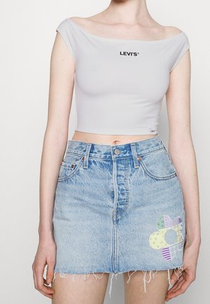 Biała krótka bluzka na ramiączkach z logo Levi's, zestawiona z jasnoniebieską mini spódnicą dżinsową z kwiatowym naszywkiem i postrzępionym dołem.