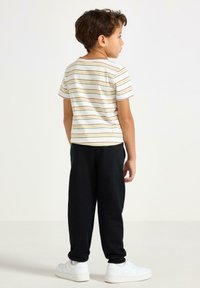 Stribet T-shirt i creme, sorte joggingbukser og hvide sneakers. T-shirten har horisontale, flerfarvede striber. Korte ærmer og rund hals.