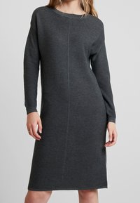 Abito grigio lavorato a maglia con maniche lunghe, scollatura rotonda e texture a coste. Presenta una linea dritta con una cucitura centrale sul davanti.