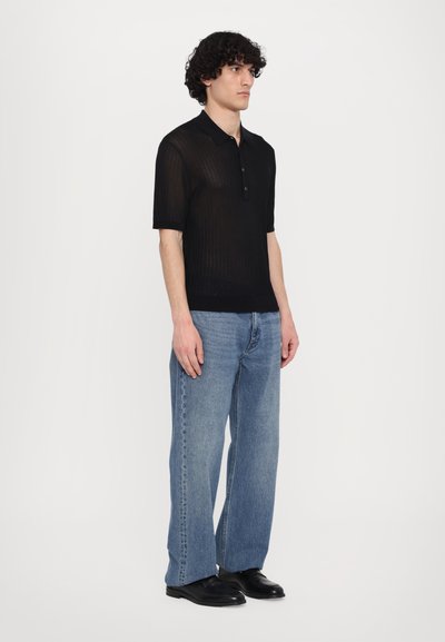 Fekete bordázott, rövid ujjú galléros póló, gombos kivágással, világoskék, egyenes szárú farmernadrággal és fekete cipővel párosítva.