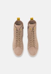 Baskets montantes beige en cuir lisse, avec des lacets ton sur ton, des œillets jaunes, une fermeture éclair sur le côté et une languette de tirage jaune contrastante.