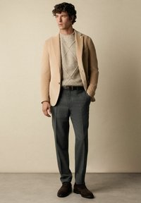 Beige korduroy blejzr přes strukturovaný světle šedý svetr, spárovaný s tmavě šedými kalhotami a hnědými botami. Jednoduchý design, přiléhavý střih.