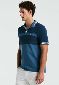 Men's polo shirt in dark blue with horizontal stripes. Features a pointed collar, three buttons, and striped accents on the sleeves.