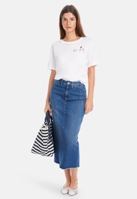 Weißes T-Shirt mit kurzen Ärmeln und bedrucktem Design, kombiniert mit einem hoch taillierten blauen Jeansrock und einer gestreiften Handtasche. Weiße flache Sandalen mit Riemchen.