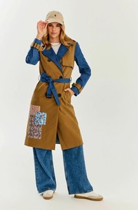 Brązowy i niebieski denimowy płaszcz trench z paskiem, w luźnym kroju, z kwiatową naszywką z przodu. Połączony ze spodniami typu wide-leg.