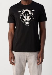 Černé bavlněné tričko s velkým bílým motivem tygra na přední straně. Krátké rukávy a kulatý výstřih; hladká textura materiálu.