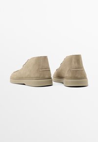 Chaussures de cheville en daim beige avec une semelle en caoutchouc robuste, un bout arrondi et un design de lacets minimaliste, comportant de légères accents de couture sur le dessus.
