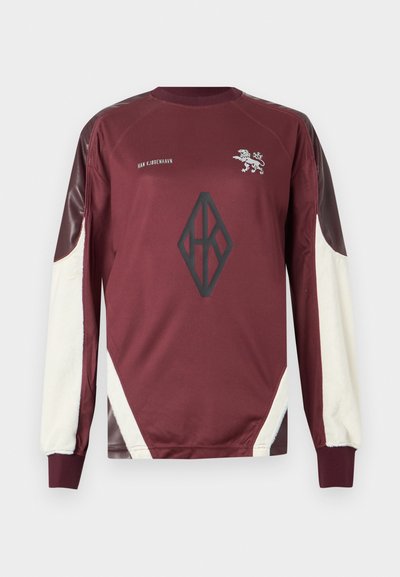 Sweat-shirt bordeaux à manches longues avec accents crème, arborant un logo de lion et un graphique géométrique sur le devant. Tissu doux avec une finition texturée.