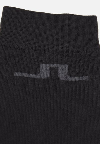 Calcetines de punto negros con puño acanalado. Presentan un discreto diseño de logo gris cerca del tobillo. El material parece suave y elástico.