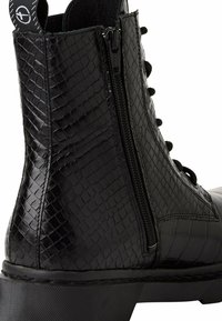 Bottine noire à texture crocodile, avec fermeture éclair latérale, lacets et semelle épaisse, dotée d'une languette en tissu de marque à l'arrière.
