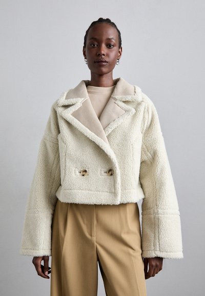 Valkoinen cropped takki pehmeästä, teksturoidusta kankaasta, kaksiriviset napit ja kontrastivärinen beige kaulus.