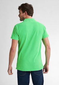 Polo verde cu manșă scurtă, fabricat din bumbac, având un guler clasic, fante laterale și o textură netedă, simplă. Purtați-l cu blugi albaștri.