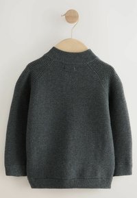 Szary dziany sweter z wysokim kołnierzem, prążkowaną teksturą i raglanowymi rękawami, wiszący na drewnianym wieszaku na neutralnym tle.
