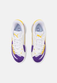 Adidași albi cu accente violet și galben. Prezentând un material texturat, șireturi plate și o talpă interioară căptușită. Logo Puma pe lateral.