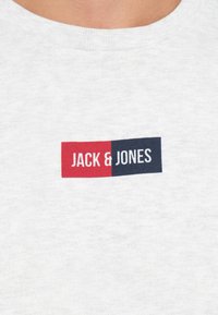 Grijze crewneck sweatshirt met een rood en marineblauw rechthoekig logo met de tekst "JACK & JONES" op de voorkant. Gemaakt van zacht katoen.