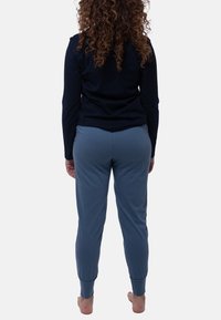 Marinblå långärmad topp och blåa sweatpants; mjukt tyg, passform vid ärmarna och elastisk midja. Utsikt bakifrån, bara fötter synliga.