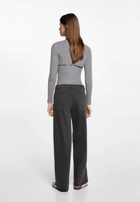 Maglia grigia a maniche lunghe con un design corto sul retro, abbinata a pantaloni ampi di colore grigio scuro con due tasche posteriori.